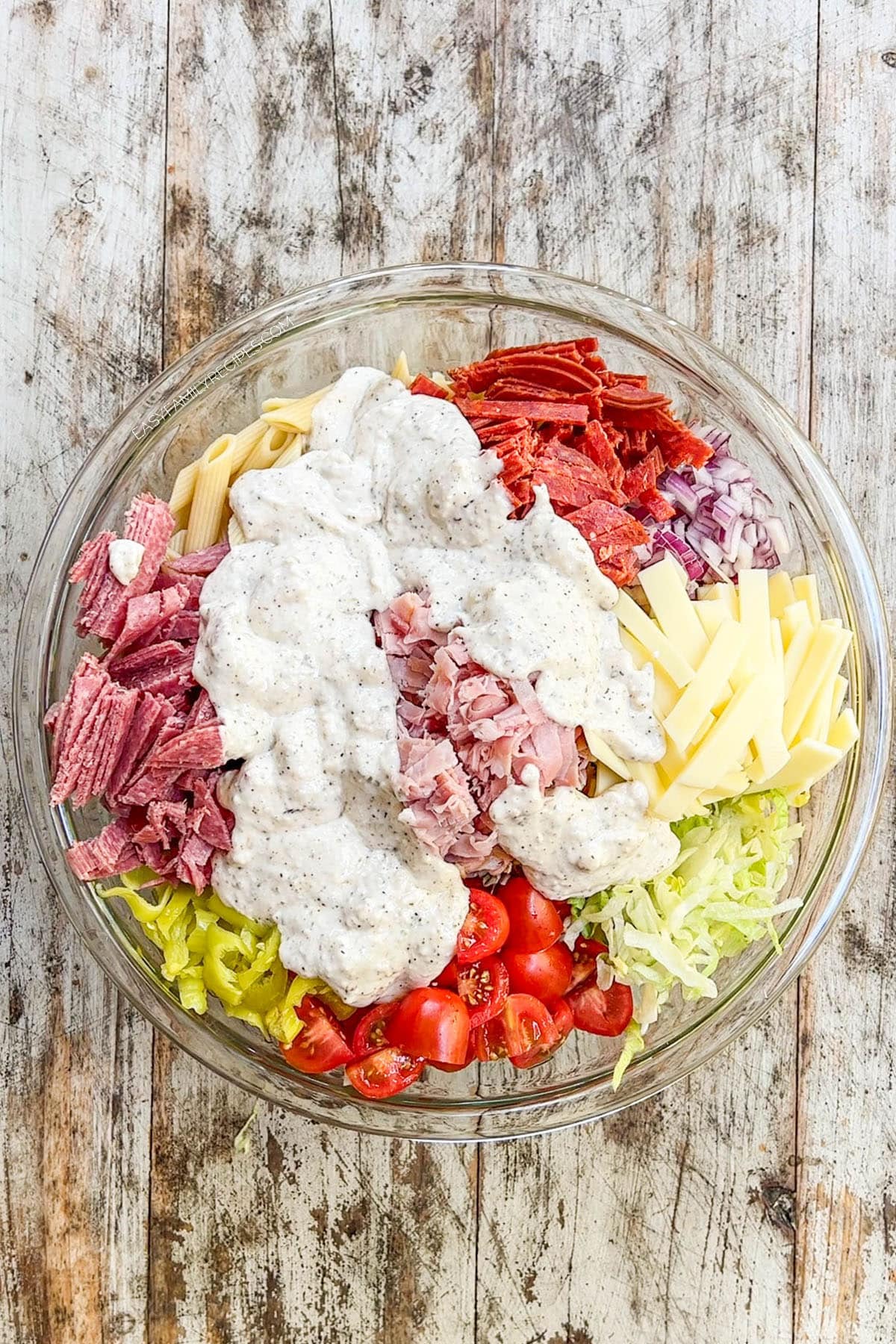 Ingredients for Italian Grinder Pasta Salad in a bowl with creamy dressing drizzled over the top.