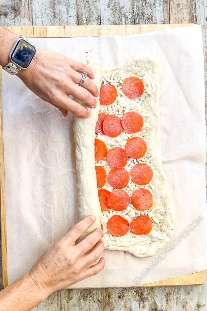 a rectangle of dough layered with pizza toppings being rolled up.