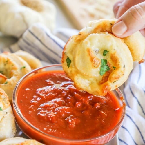 a pizza roll being dipped into a bowl of marinara sauce.