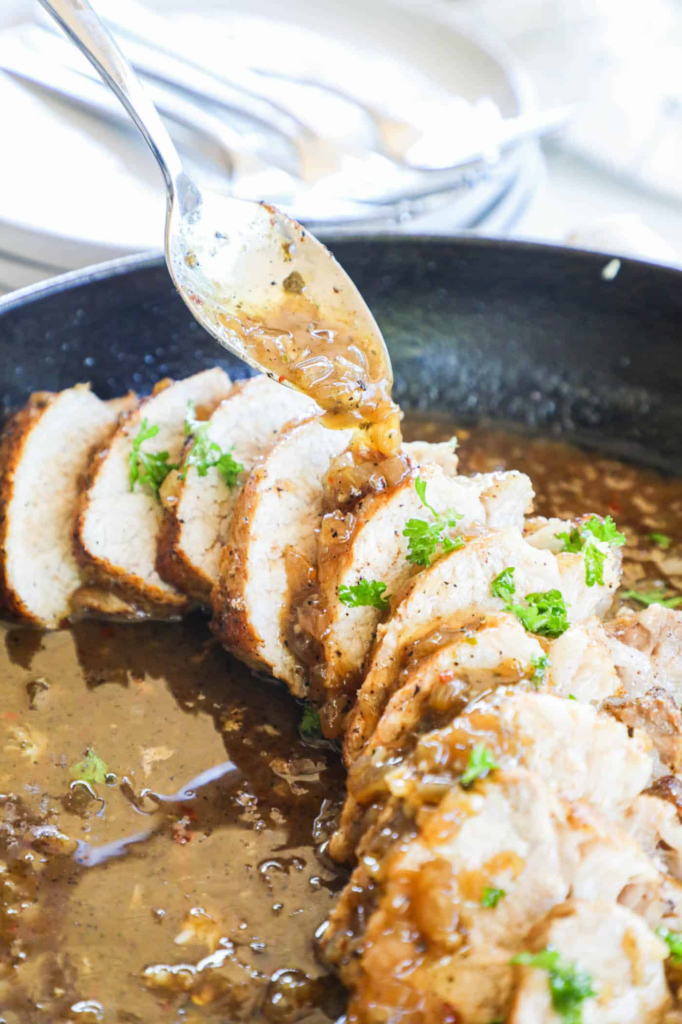 pork tenderloin in a skillet being drizzled with gravy