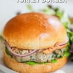 A turkey burger with aioli, red onion, and lettuce. The burger is on a white plate. The text reads, "Tuscan Turkey Burgers."