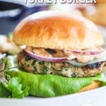 A turkey burger inside a soft bun with aioli, red onion, and lettuce. The burger is on a white plate. The text reads, "Tuscan Turkey Burgers."
