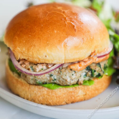 A turkey burger inside a soft bun with aioli, red onion, and lettuce. The burger is on a white plate with a white background.
