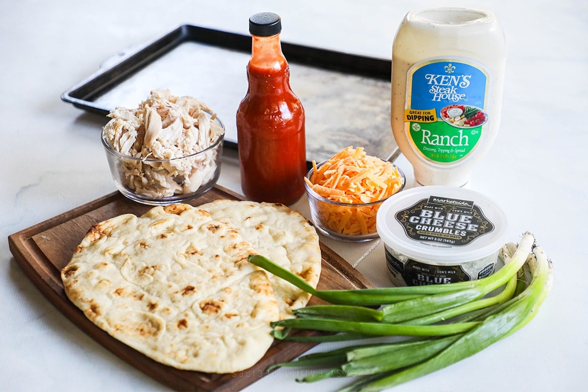 Ingredients for buffalo chicken flatbread including naan flatbread, buffalo sauce, cheddar cheese, blue cheese, ranch dressing and chicken.