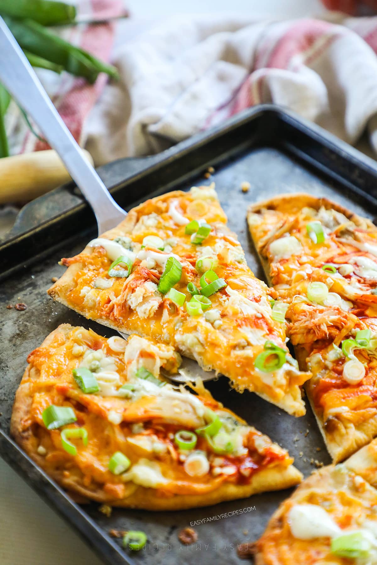 A piece of buffalo chicken flatbread being lifted out of the pan with a spatula. 