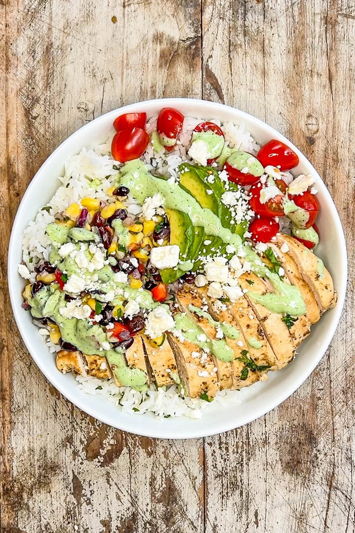 An assembled chicken baja bowl in a white dish on a distressed wooden background.
