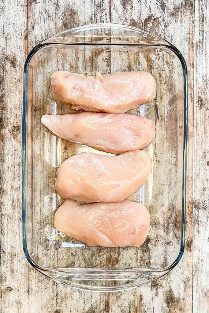 four chicken breasts lined in a baking dish.