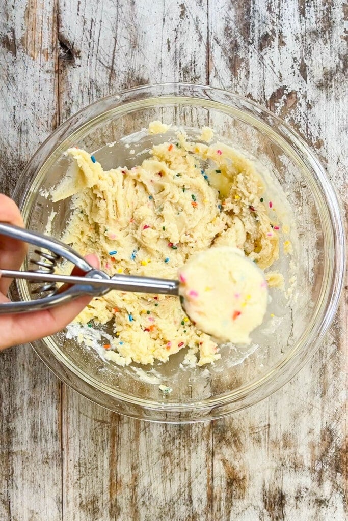 birthday cake cookie dough being scooped out of a mixing bowl.