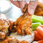 A hand dipping an Asian Zing Wing into dipping sauce. The text reads, "Asian Zing Wings."