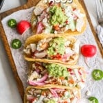 Top view of a row of Baja Chicken Tacos on a parchment-lined cutting board. The text reads, "Baja Chicken Tacos."