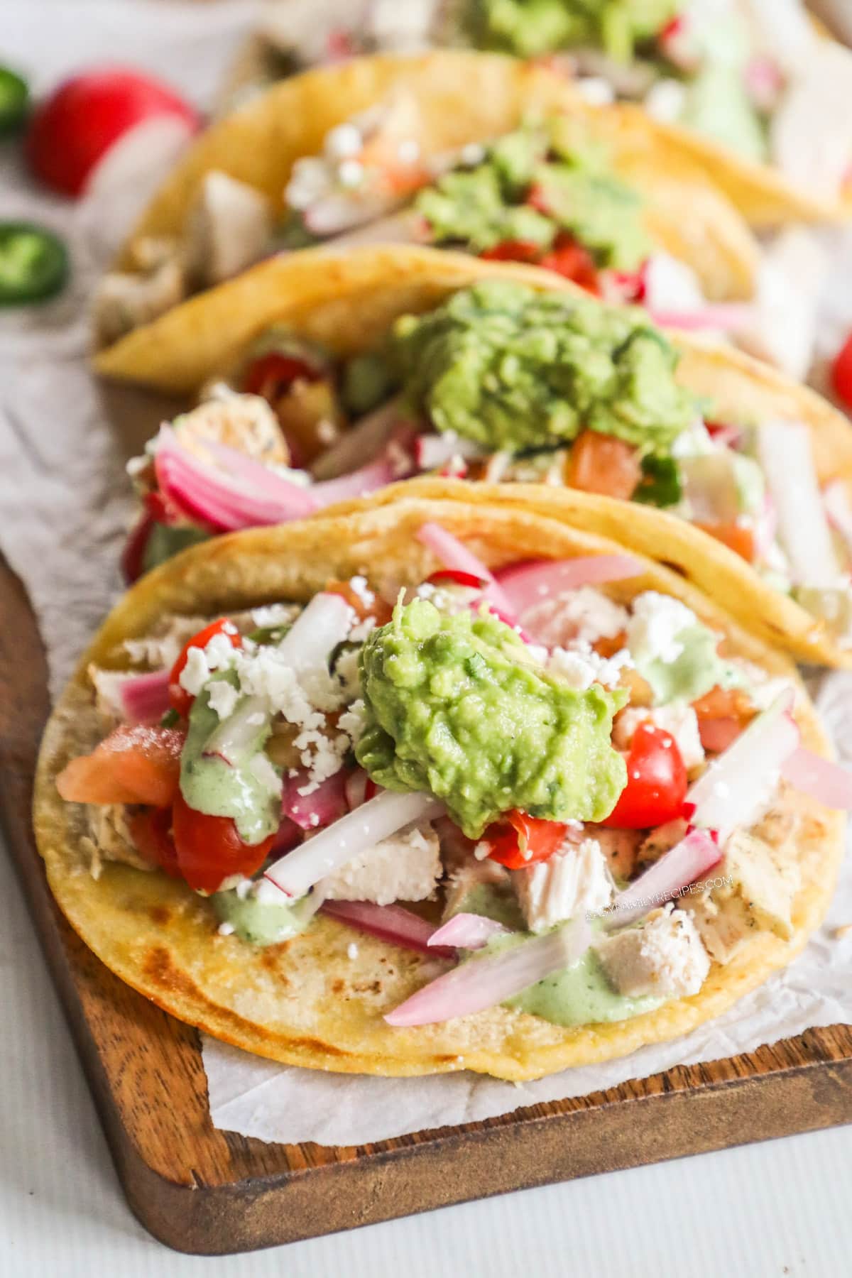 A row of Baja Chicken Tacos on a parchment-lined cutting board. 