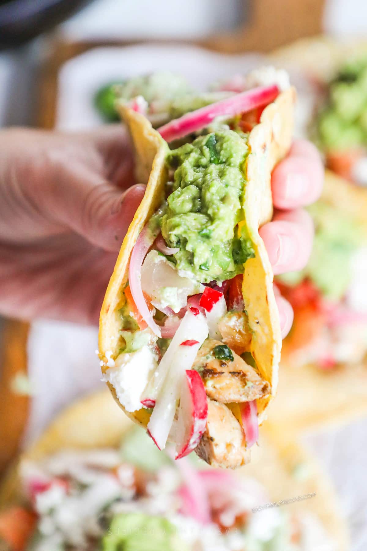 A hand holds a single Baja Chicken Tacos, ready to eat.