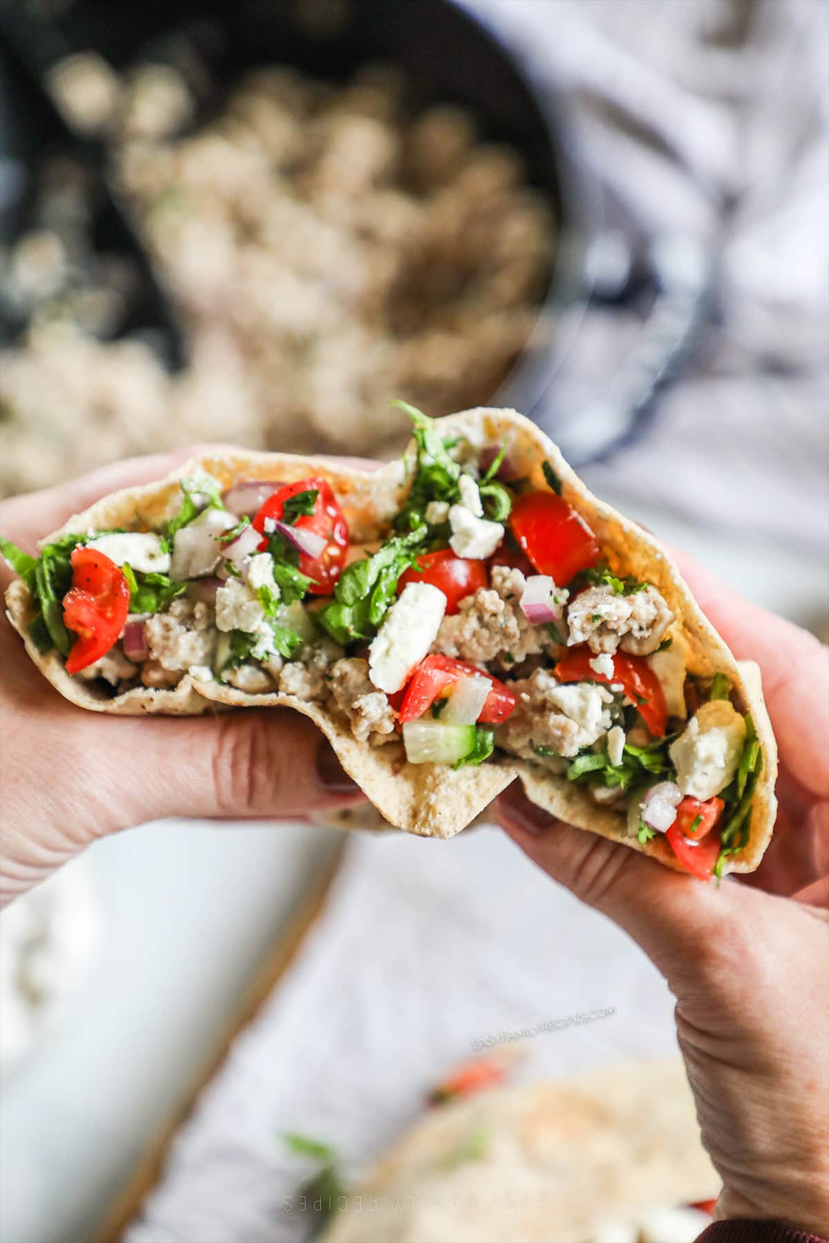 Hands holding a stuffed Mediterranean ground chicken pita.