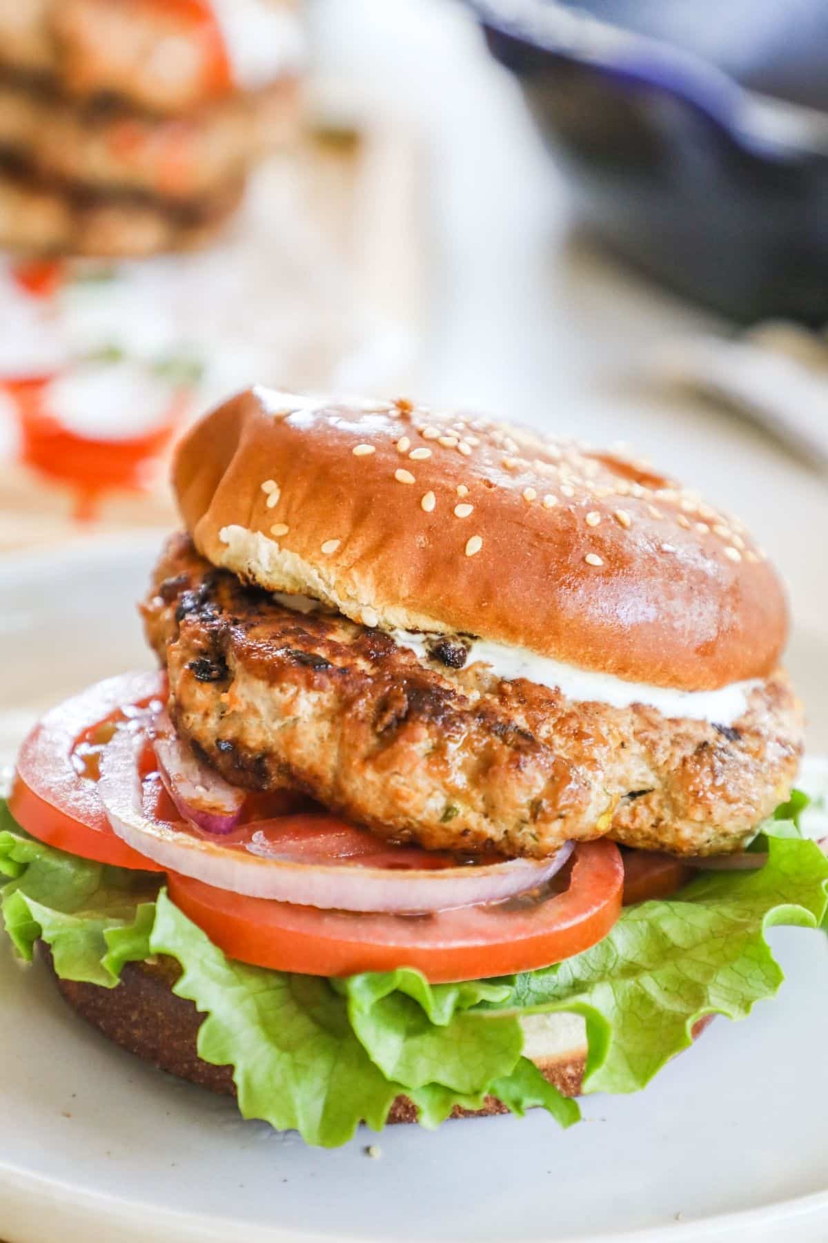 buffalo chicken patty on a bun with ranch, lettuce, tomato, and onion.  on a white plate