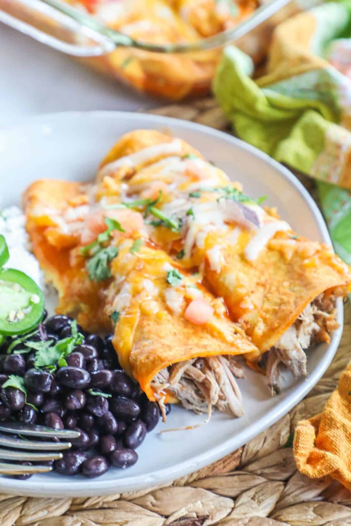 2 carnitas enchilas on a white plate with rice and beans