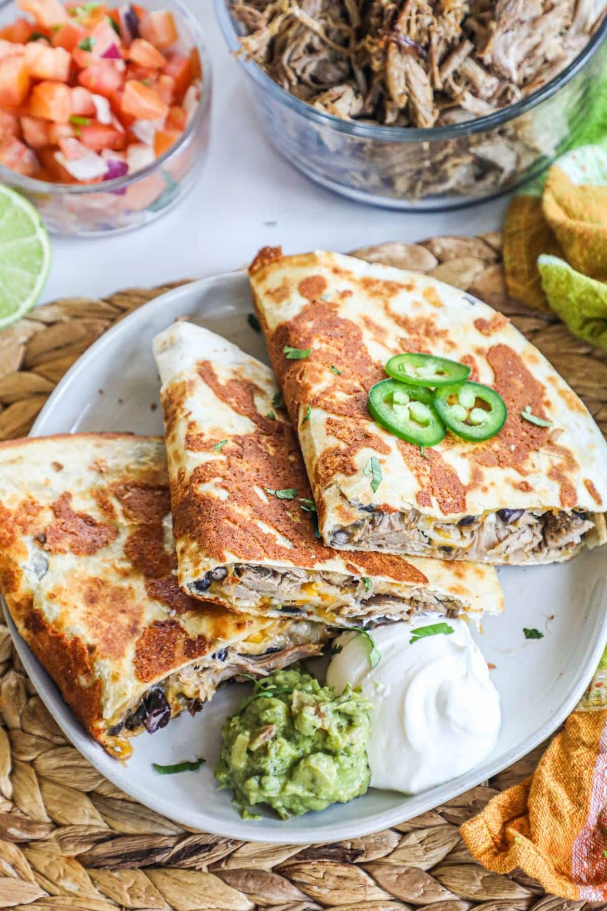 3 carnitas quesadillas on a plate with sour cream and quacamole for dipping