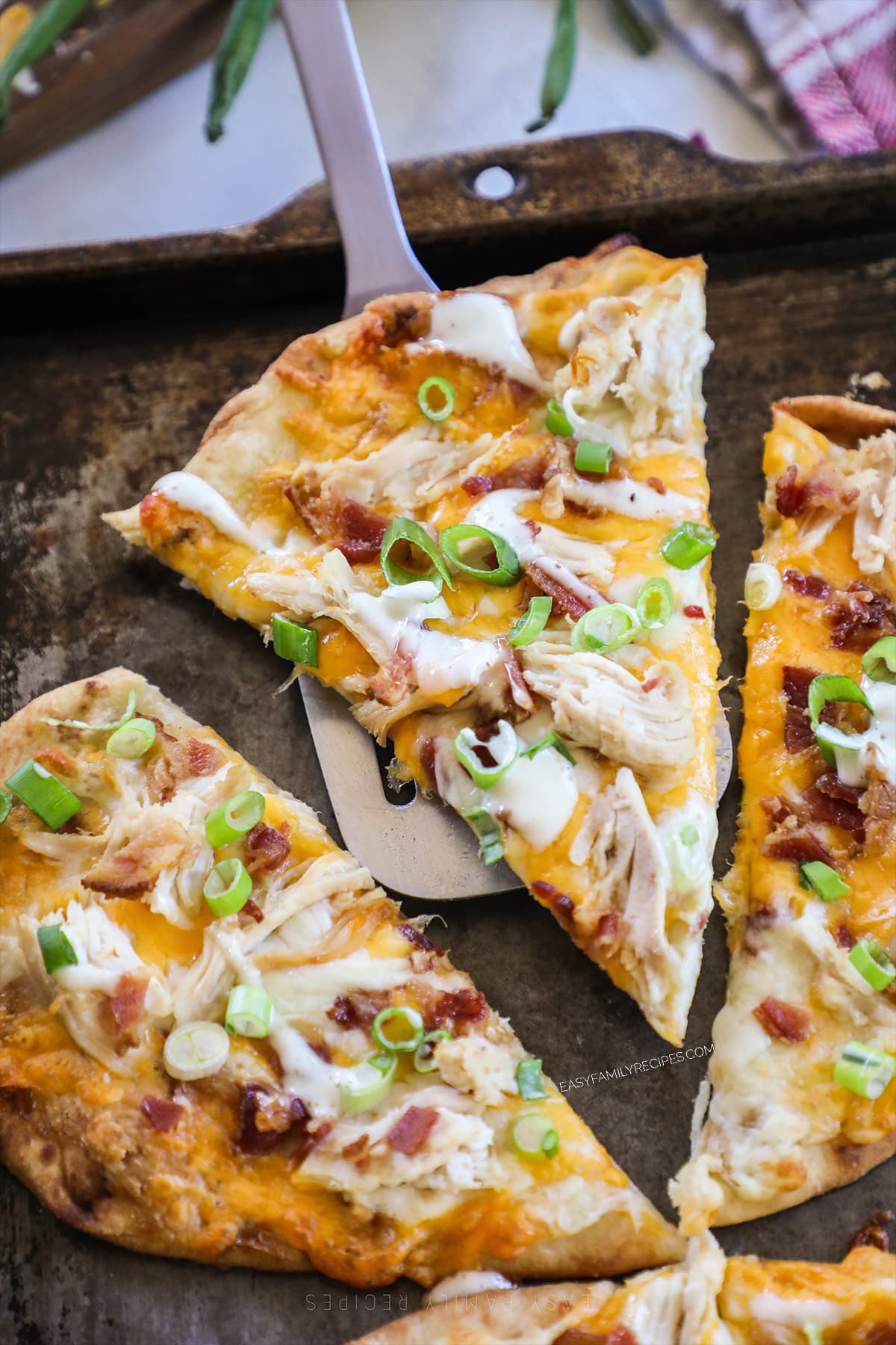 A slice of chicken bacon ranch flatbread is lifted from the pan.