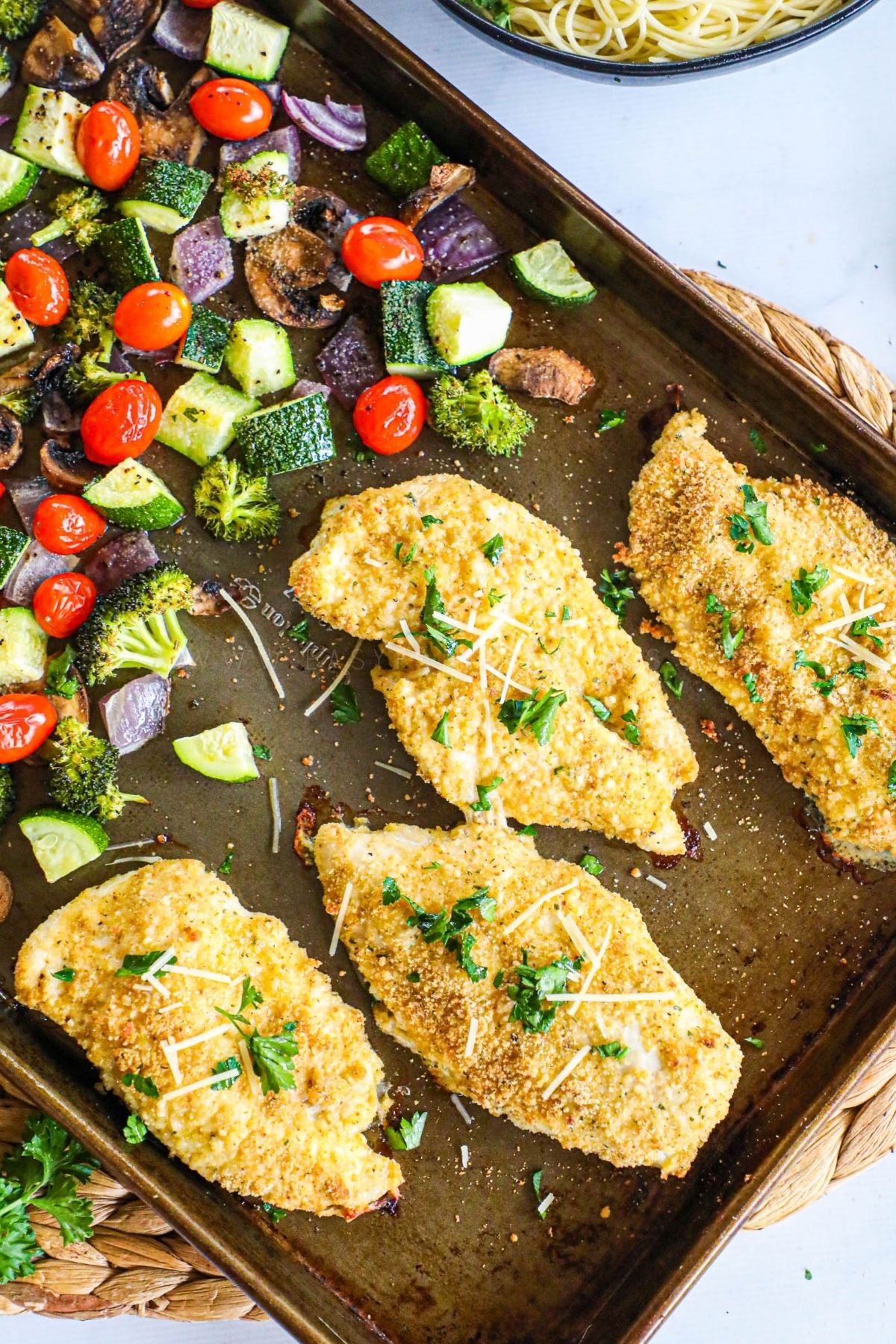 breaded chicken cutlets and mixed grilled veggies on a baking sheet