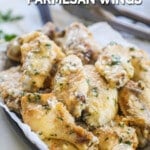 A parchment paper lined tray piled with slow cooker garlic Parmesan wings, garnished with extra cheese and herbs. Tongs are in the background. The text reads, "Crock Pot Parmesan Wings."