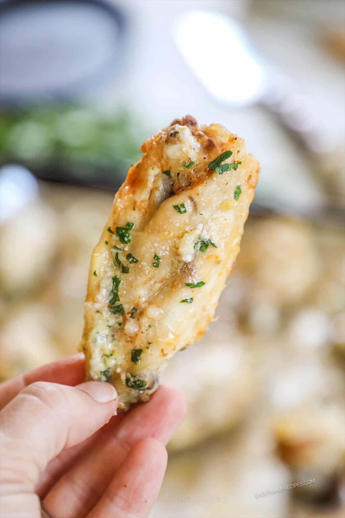 A hand holding a single slow cooker garlic Parmesan wing.