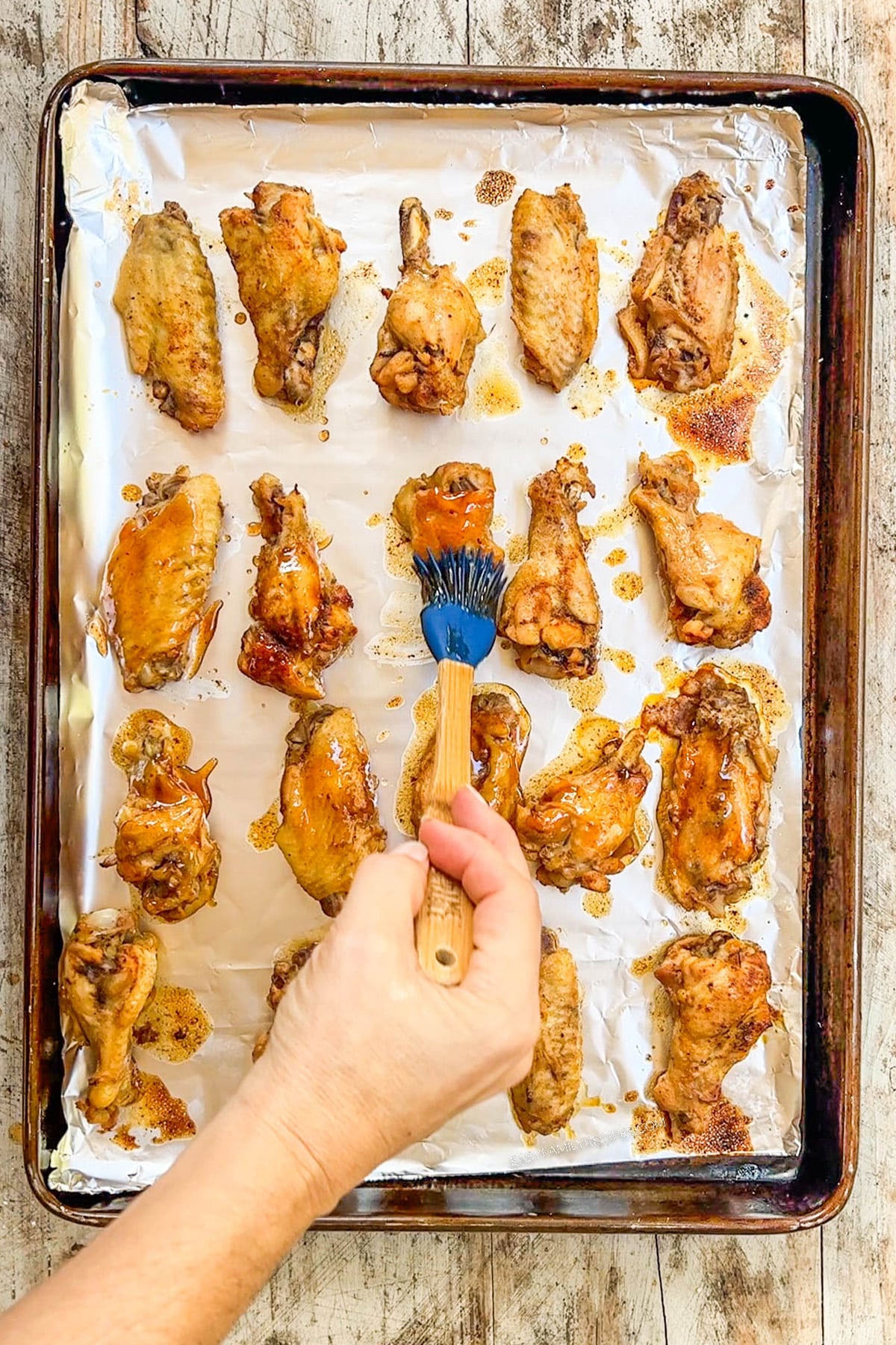 Asian Zing Wings are lined up on a cookie sheet, being brushed with sauce.