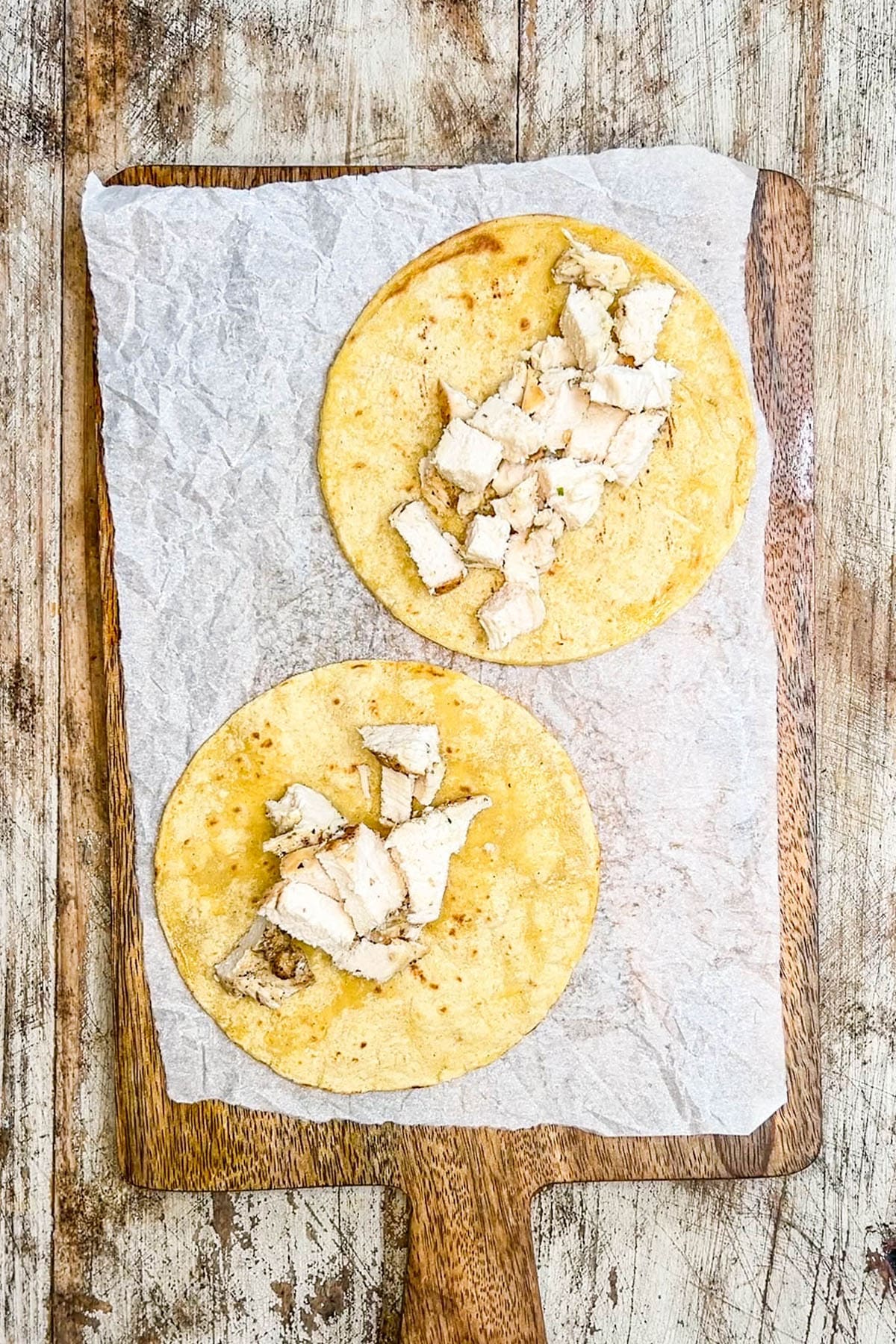 A top view of two tortillas being made into Baja Chicken Tacos. This is step 5 of the process, adding chicken.