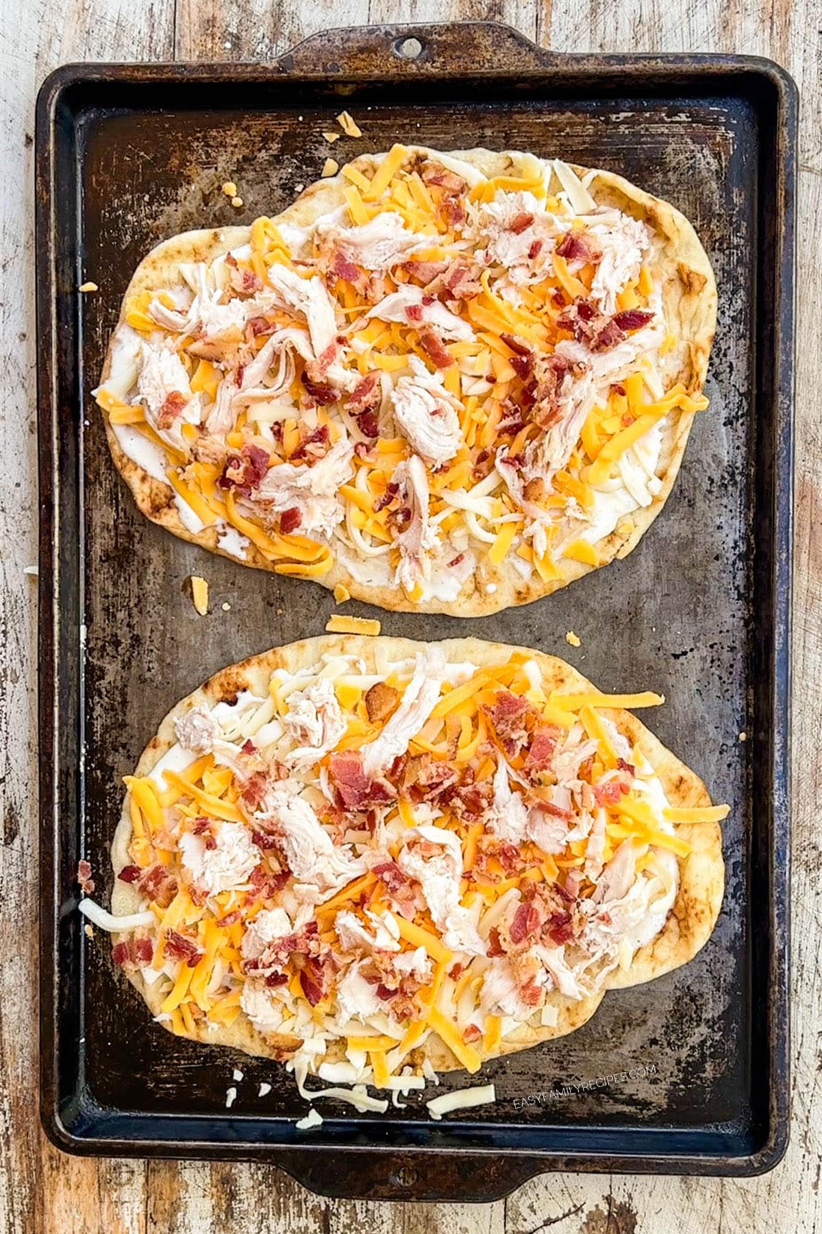 Two chicken bacon ranch flatbread pizzas on a baking sheet, ready to bake.