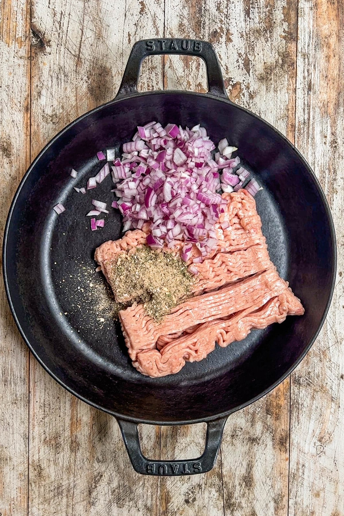 Ground chicken, onions, and spices in a skillet before cooking.