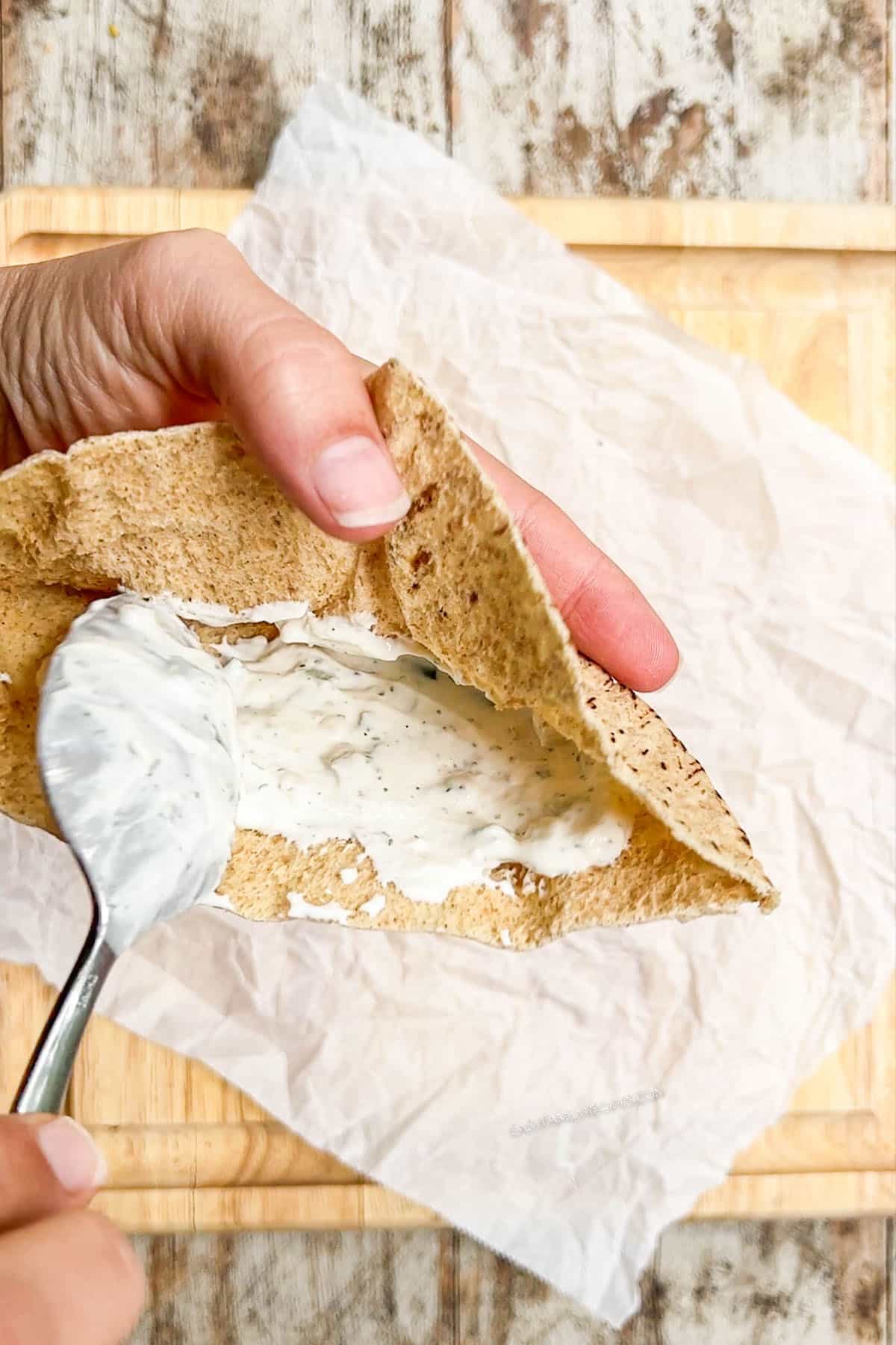 Spreading tzatziki sauce on pita.