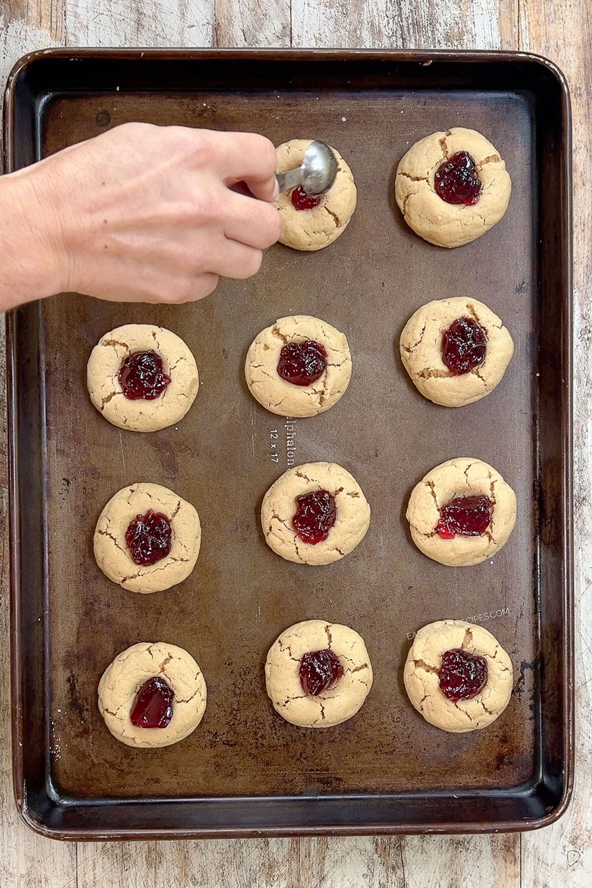 Adding jelly to Peanut Butter & Jelly Cookies on a cookie sheet.