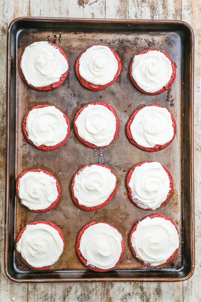 above image of frosted red velvet cookies on a baking sheet.