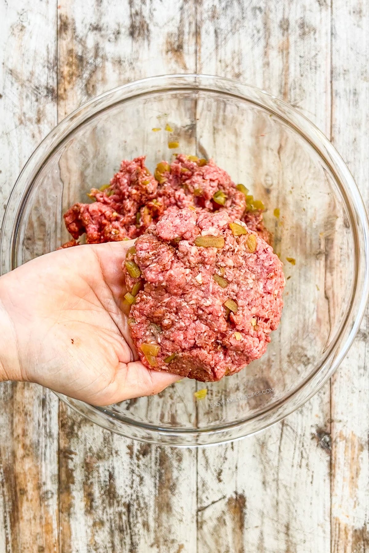 Hand holding a prepped burger patty of meat mixture.