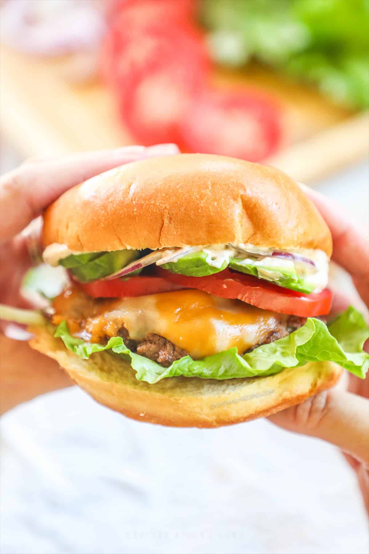 Hands holding up a big southwest burger to show the patty and all the toppings before taking a bite.