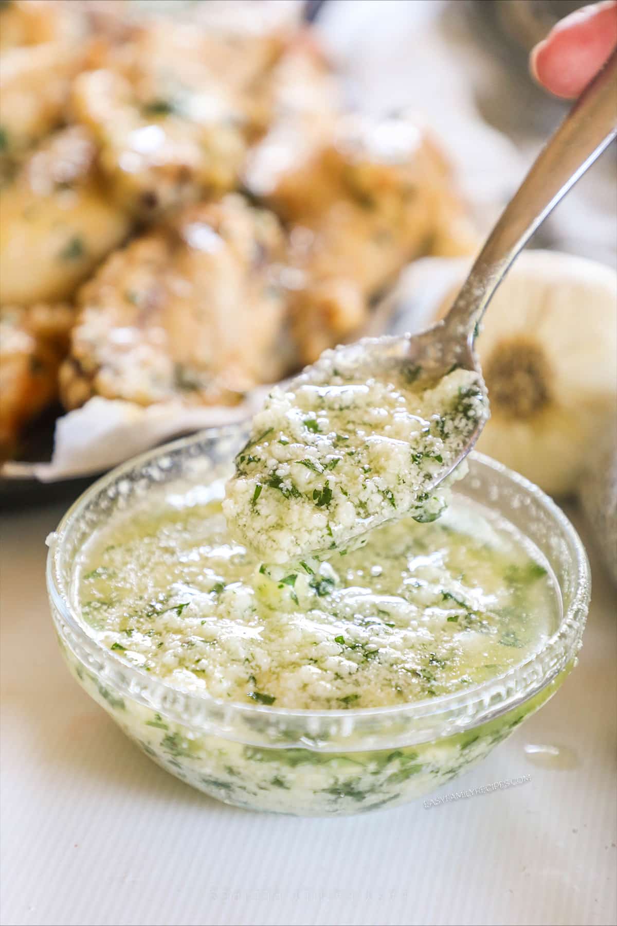 a spoon dipped into a bowl of garlic parmesan sauce for wings