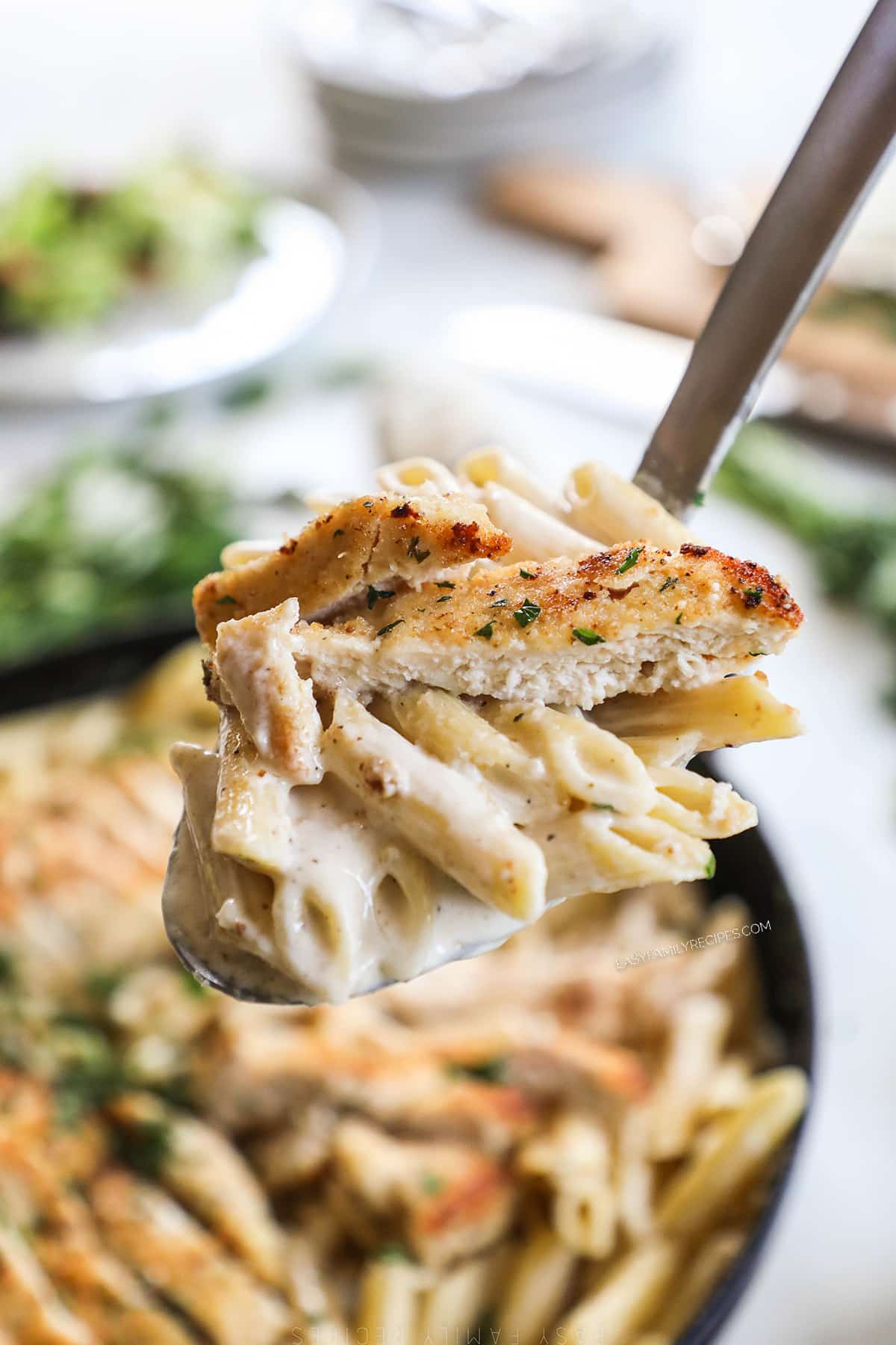 A spoonful of Garlic Parmesan Chicken Pasta is lifted from the casserole dish.