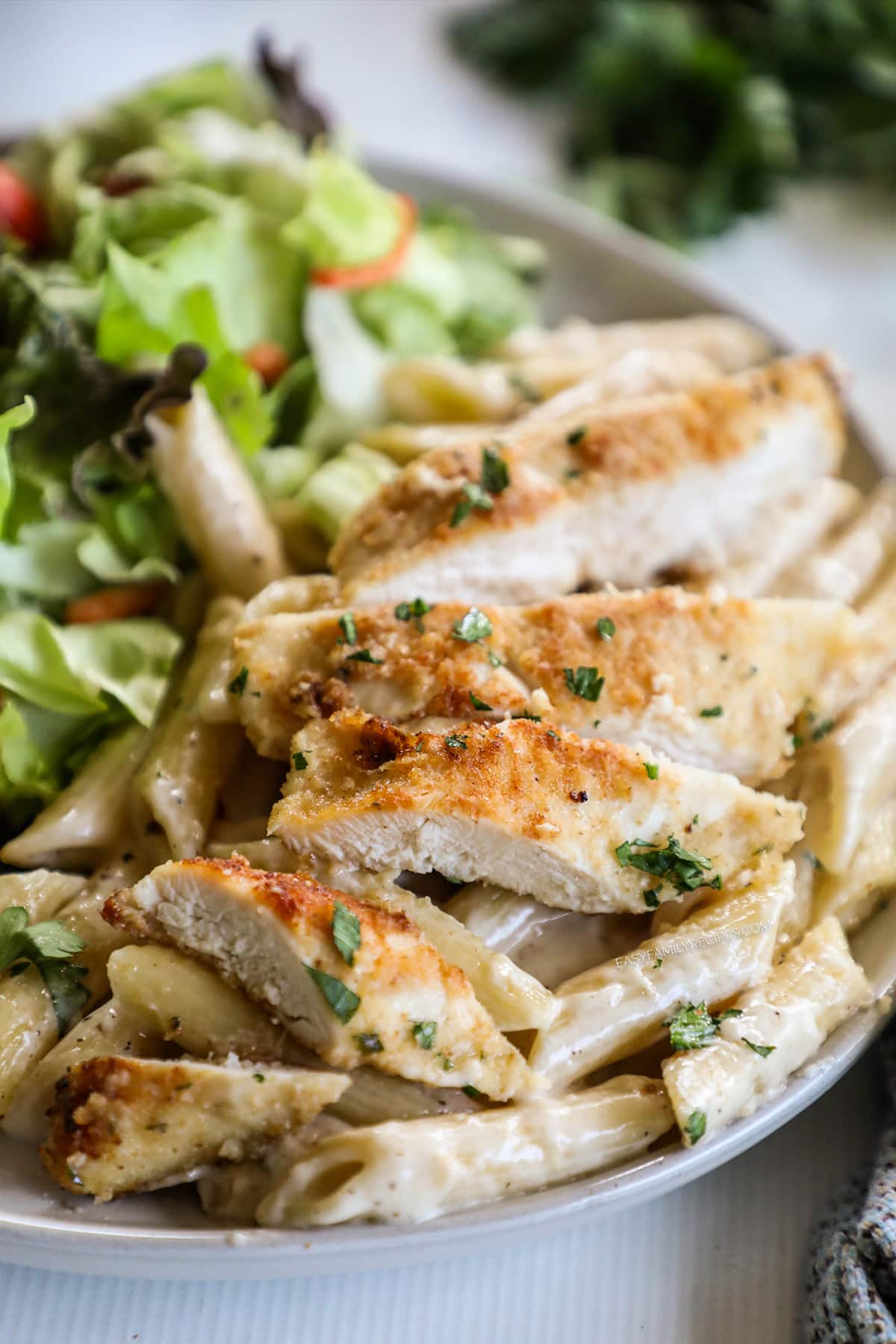 Garlic Parmesan Chicken Pasta served on a white plate with a green salad on the side.