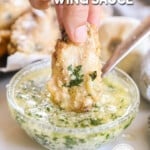 a chicken wing being dipped into a bowl of garlic parmesan sauce for wings.