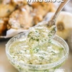 a spoon being dipped in a bowl of homemade garlic parmesan wing sauce.