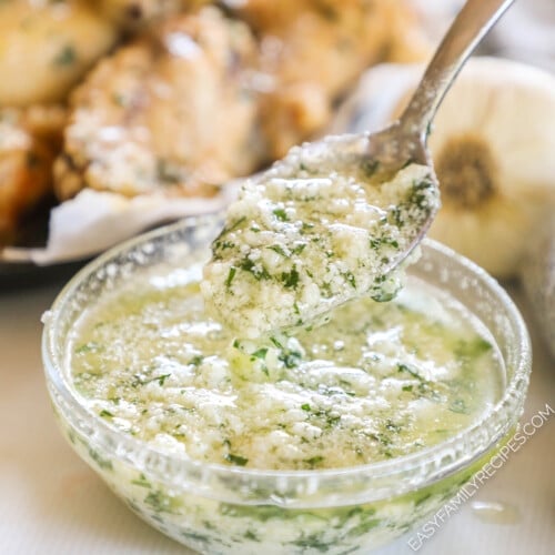 a spoon being dipped into a bowl of parmesan garlic wing sauce.