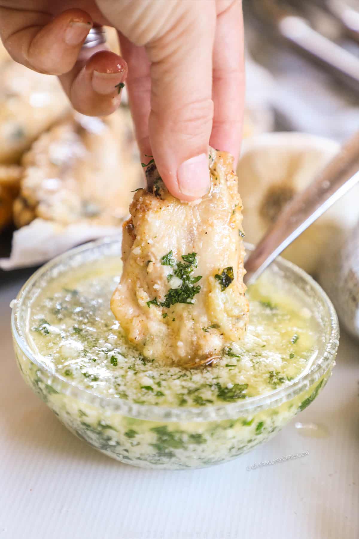 A chicken wing being dipped into garlic parmesan wing sauce. 