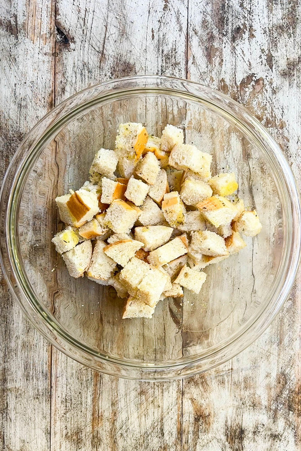 A clear glass bowl with chunks of French bread that will be made into croutons for arugula burrata salad.