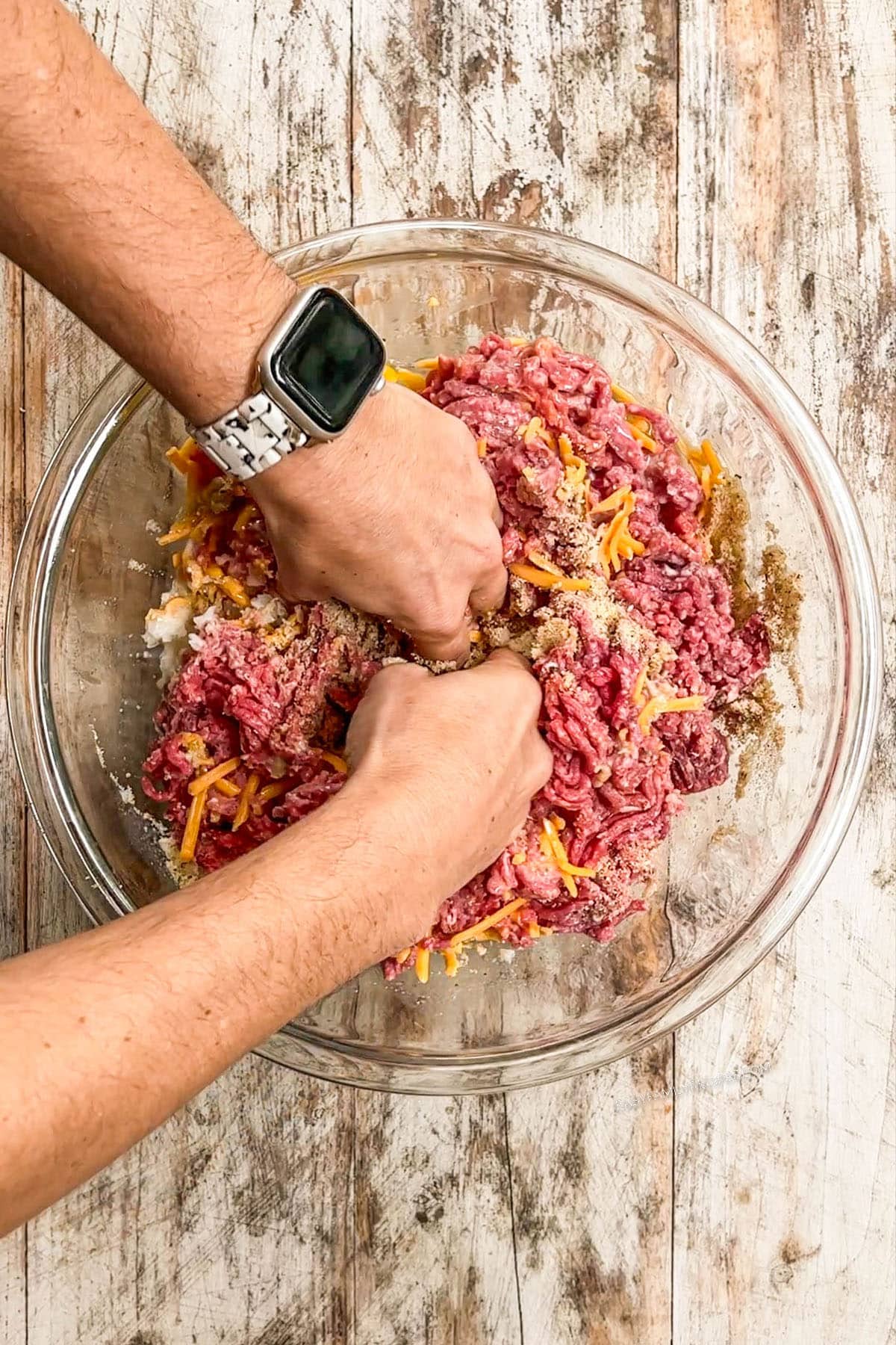 Hand mixing meat mixture in a bowl.