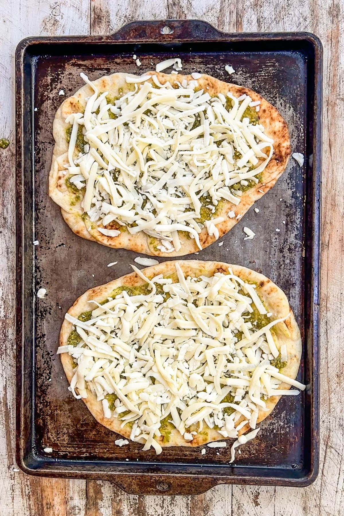 Shredded cheese added on top of a flattop with pesto.