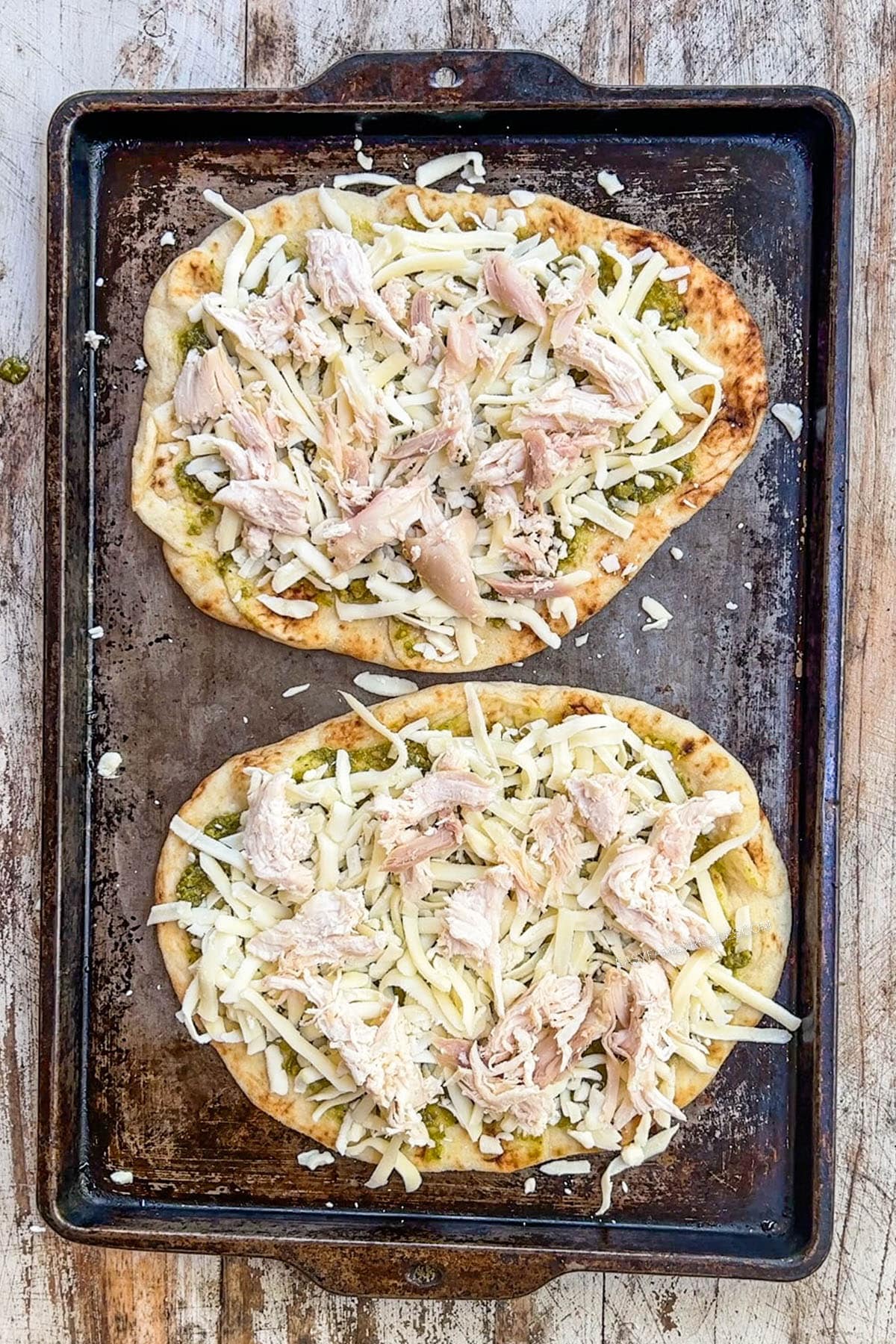 Shredded chicken on top of cheese on a flatbread.