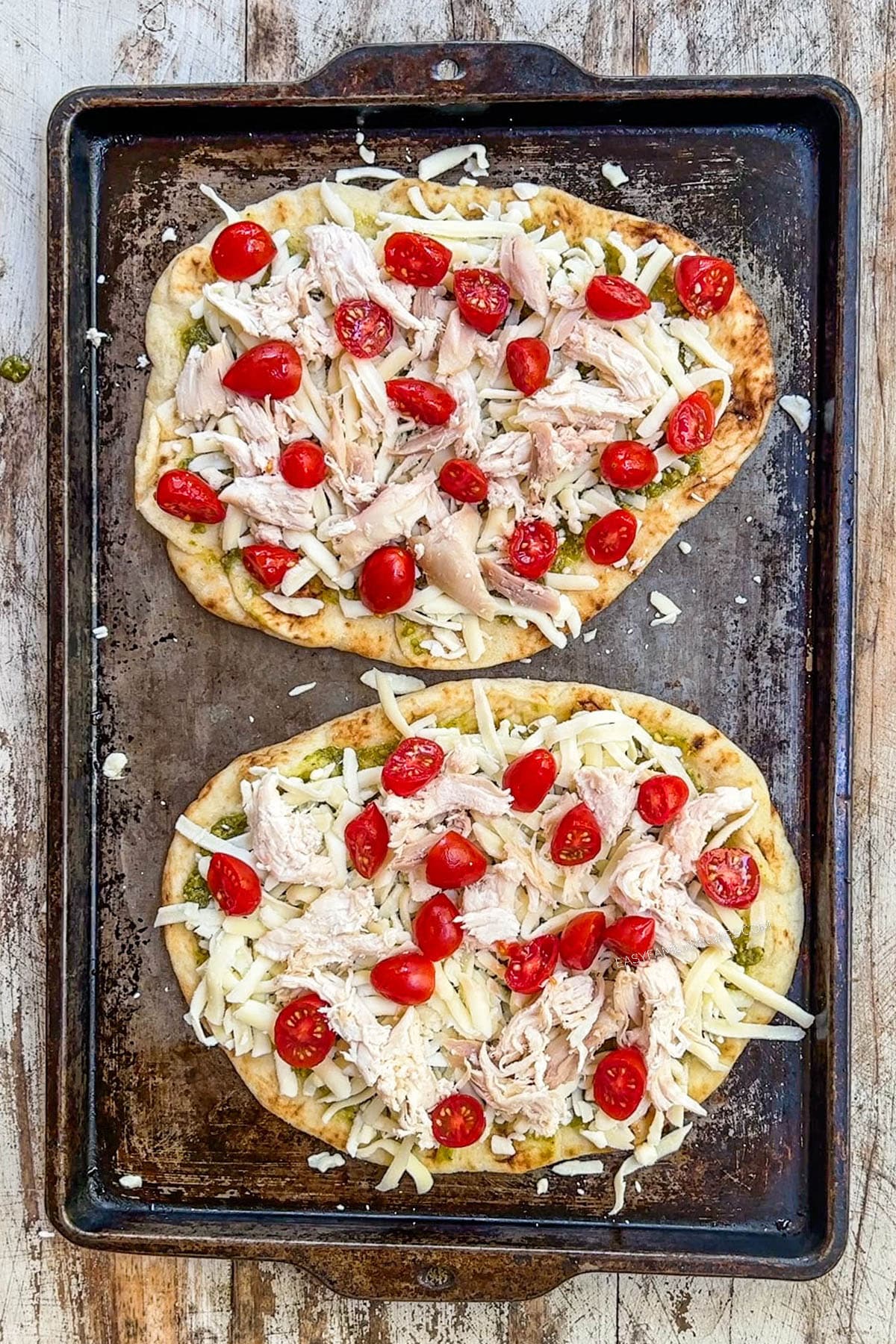 Fresh tomatoes added to a chicken pesto flatbread before baking.