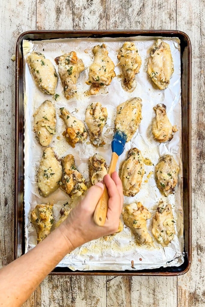 chicken wings on a baking sheet being brushed with garlic parmesan wing sauce. 