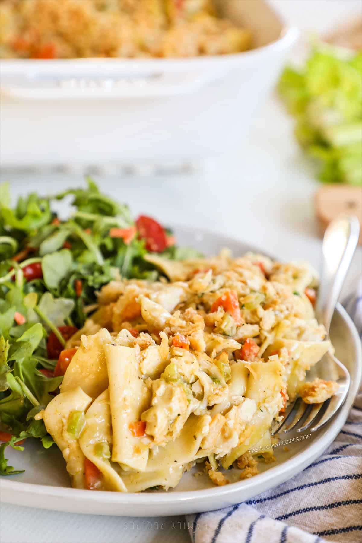 A serving of Chicken Noodle Casserole on a white plate with a salad served alongside.