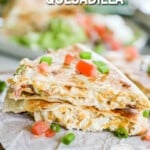 Two wedges of Chicken Bacon Ranch Quesadillas on a piece of white parchment paper with red peppers and scallions for garnish. The text reads, "Chicken Bacon Ranch Quesadilla"