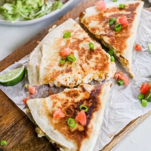 Chicken Bacon Ranch Quesadillas on a piece of parchment paper with lime wedges and veggies scattered around.