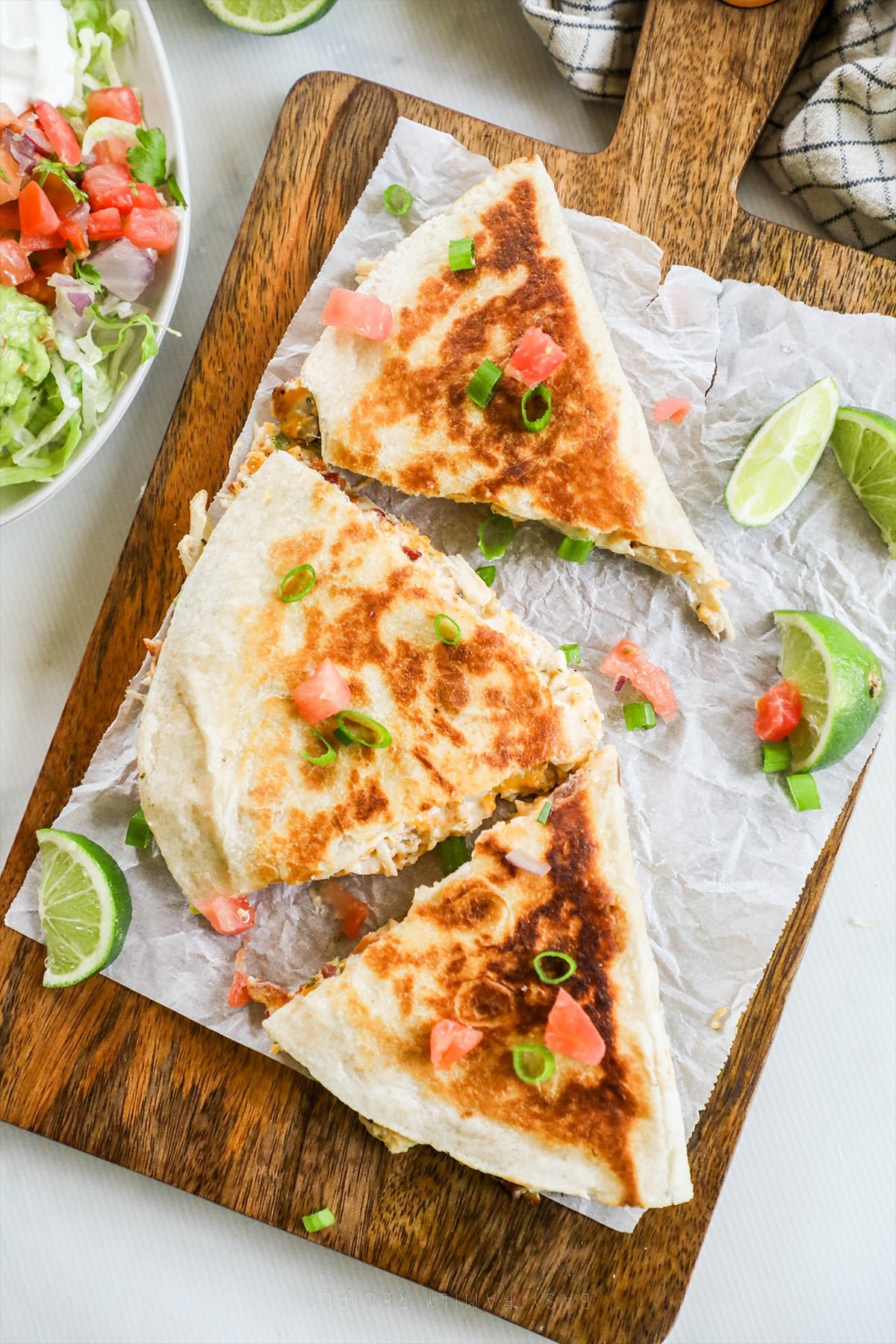 A top view of Chicken Bacon Ranch Quesadillas on a piece of parchment paper with lime wedges and veggies in the background.